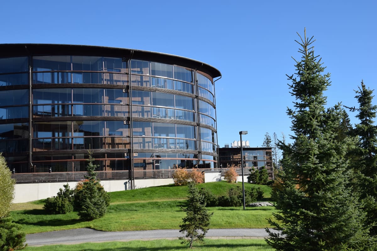 A modern building with a curved glass facade, surrounded by a landscaped area with trees and a pathway.