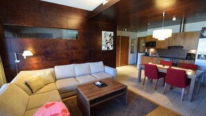Un salon moderne avec un canapé, une table basse et un coin repas comprenant des chaises, et une cuisine en arrière-plan.
