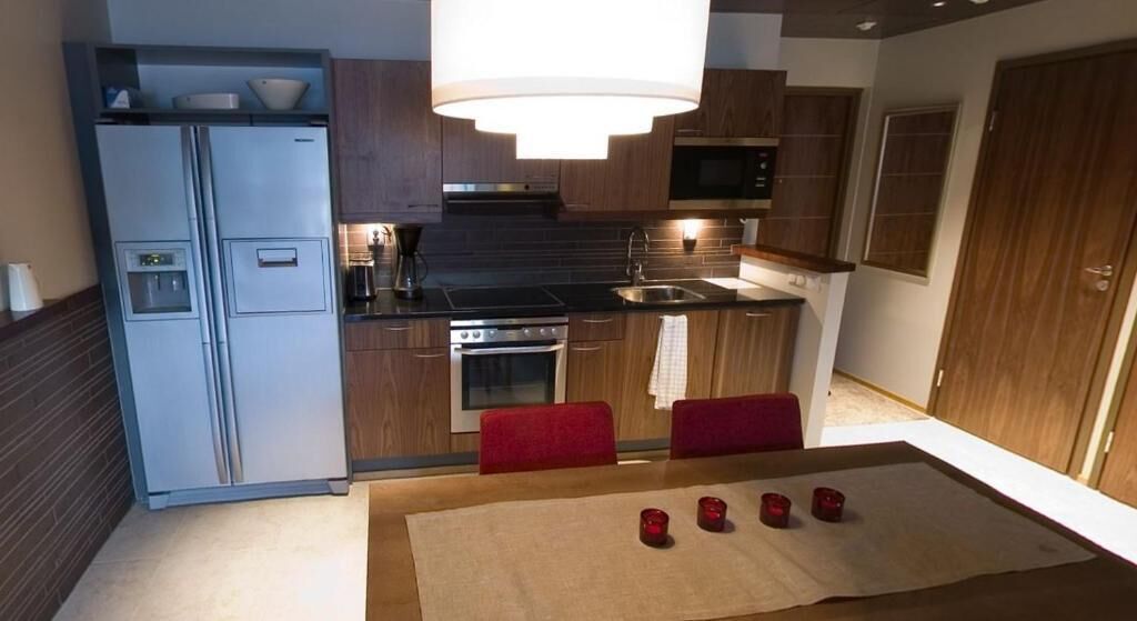 Cocina moderna con refrigerador, microondas, estufa y lavaplatos integrados. Hay dos sillas rojas y una mesa con velas.