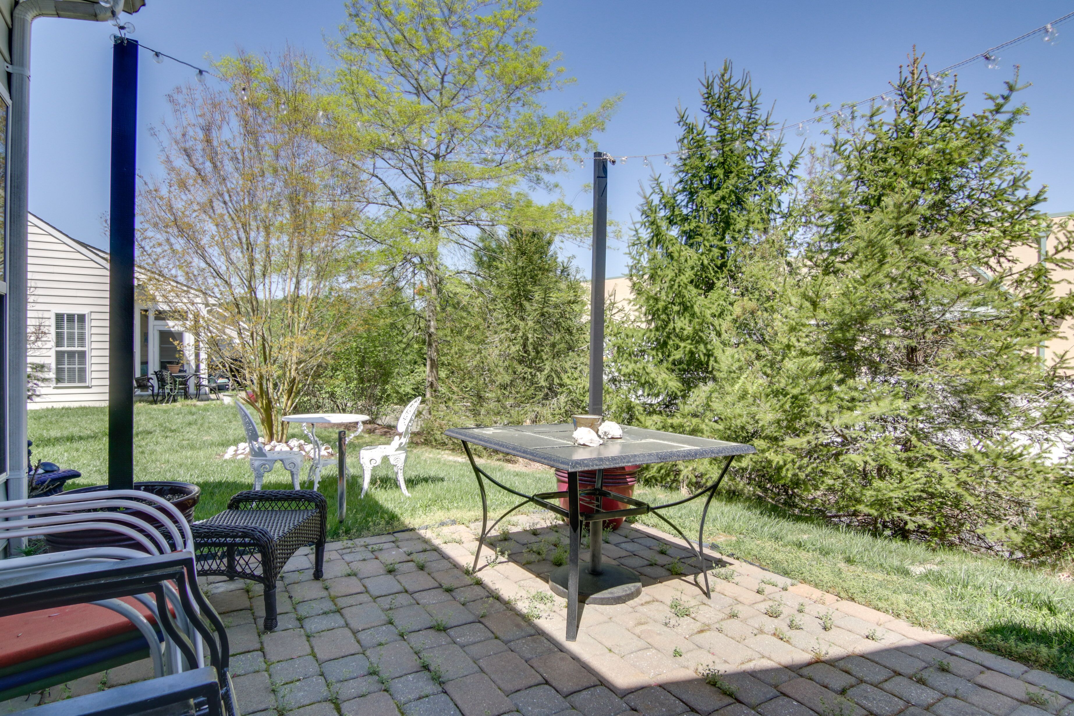 Eine Terrasse mit Tisch und Stühlen, umgeben von Grünpflanzen und einem Haus im Hintergrund.