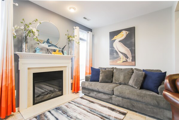 Een woonkamer met een open haard, een bank en een schilderij van een pelikaan.