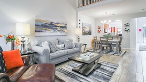 Een ruime woonkamer met een grijze bank, een salontafel en een eethoek met een houten tafel en stoelen.