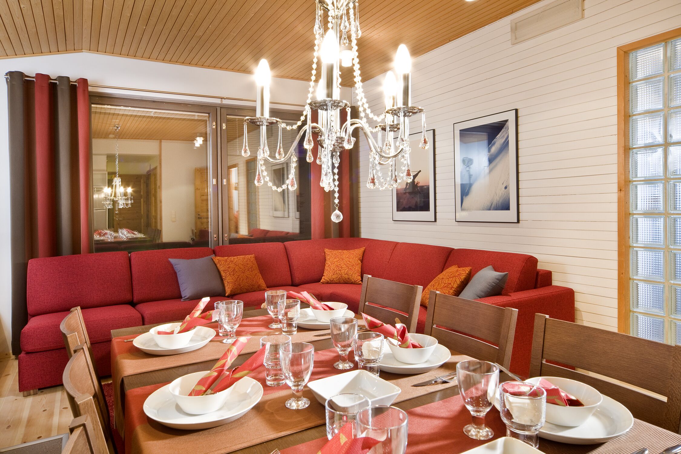Un coin repas avec un canapé rouge, des chaises en bois, un lustre et une table mise pour le repas.