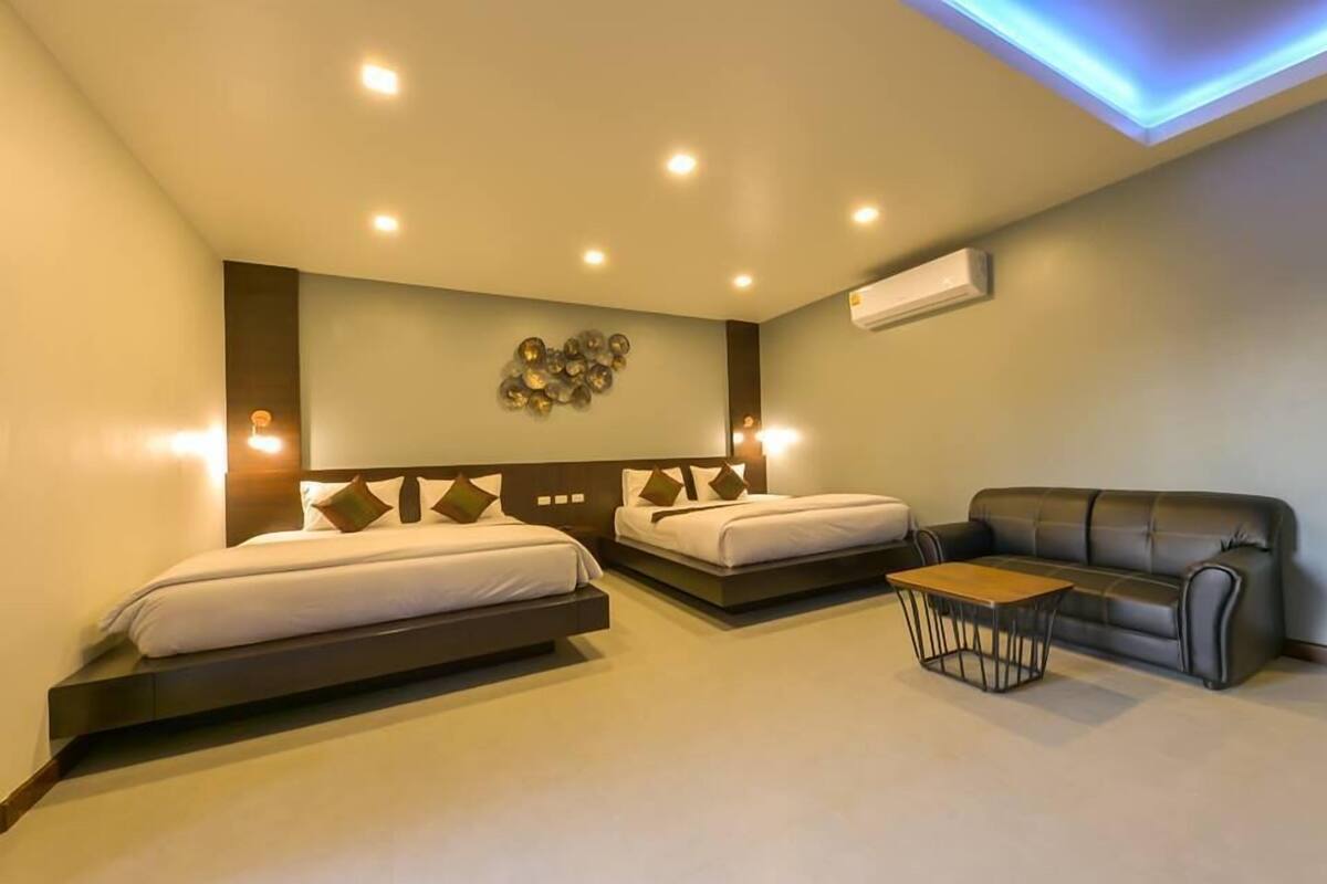 A modern hotel room with two beds, a sofa, and a small table.