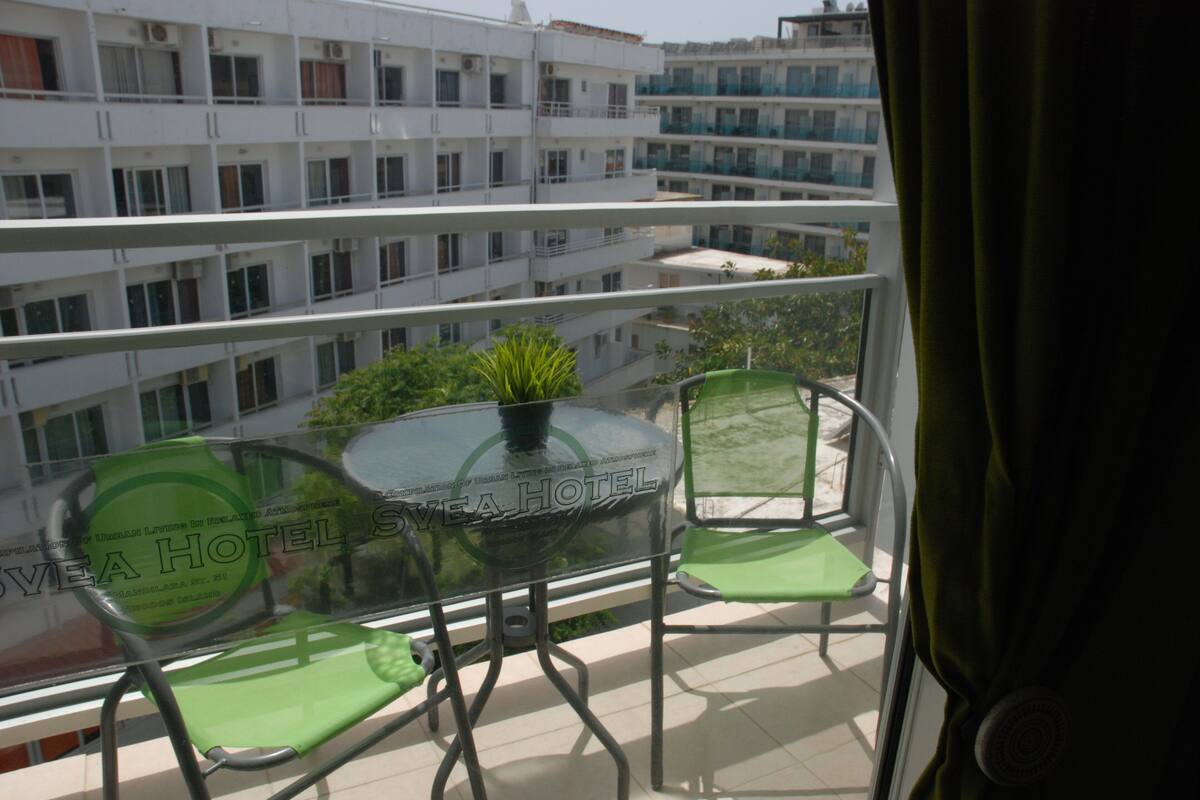 A balcony with a glass table and two chairs, overlooking a building with multiple balconies.