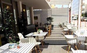 An outdoor dining area with striped flooring, white tables, and chairs. - Sveas Hotel (Rhodes)