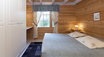 Quarto de cabana de madeira com cama, mesa de cabeceira com abajur, janela com cortinas e porta.