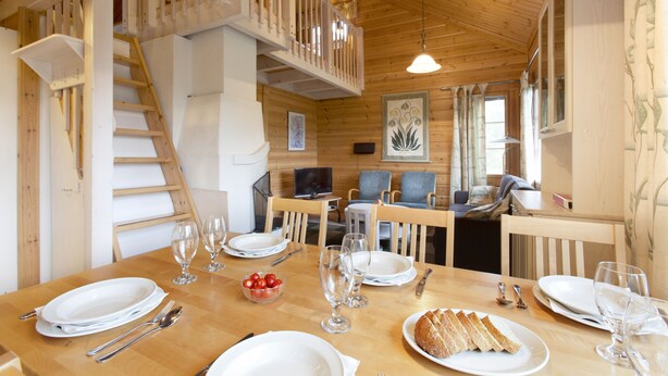 A dining area with a wooden table set for a meal, a staircase, and a living area with seating.