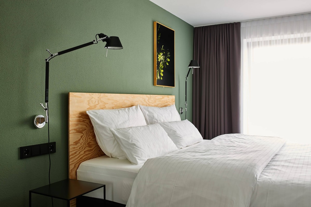 Ein ordentlich bezogenes Bett mit weißen Bettwäsche, ein Holzkopfschild und eine schwarze Stehlampe auf einem Nachttisch.