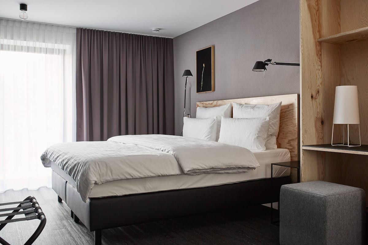 Ein modernes Schlafzimmer mit Bett, Nachttisch, Lampe und Blick ins Freie.