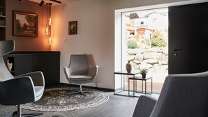 A modern living room with a grey armchair, a round rug, and a view of a garden through a sliding door. - Winterfeld Guest House Bodenmais (Bodenmais)