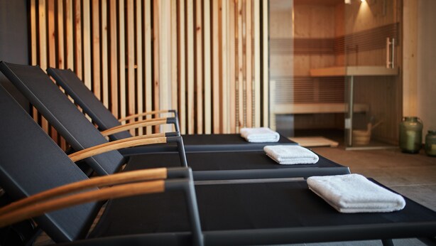 A row of black lounge chairs with wooden armrests, a wooden slat wall, and a glass door leading to a room with a shower. - Winterfeld Guest House Bodenmais (Bodenmais)
