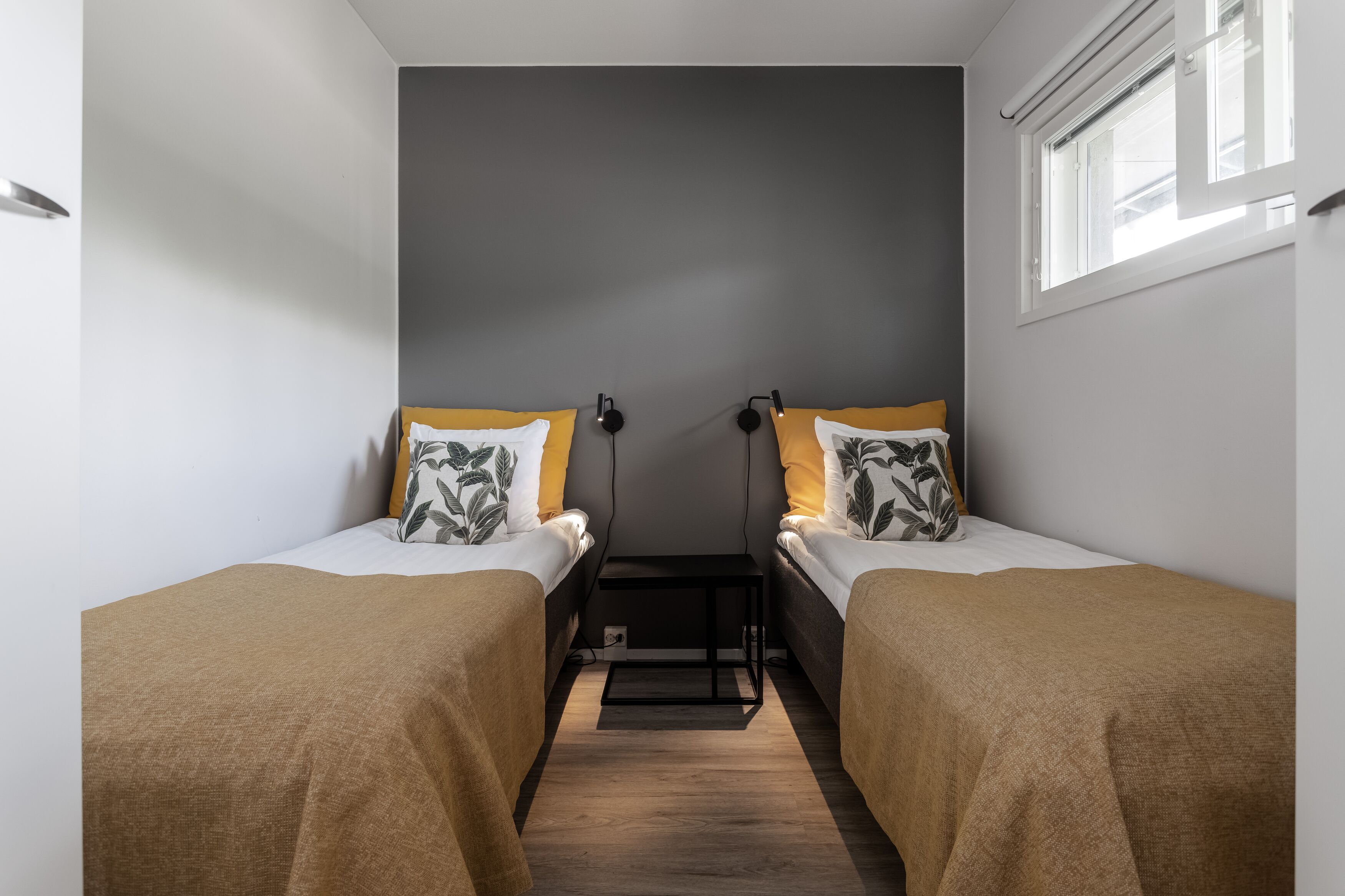 Habitación doble con dos camas, cada una con cubrecama marrón y almohada con diseño de hojas. Entre las camas hay una mesita de noche pequeña y negra.