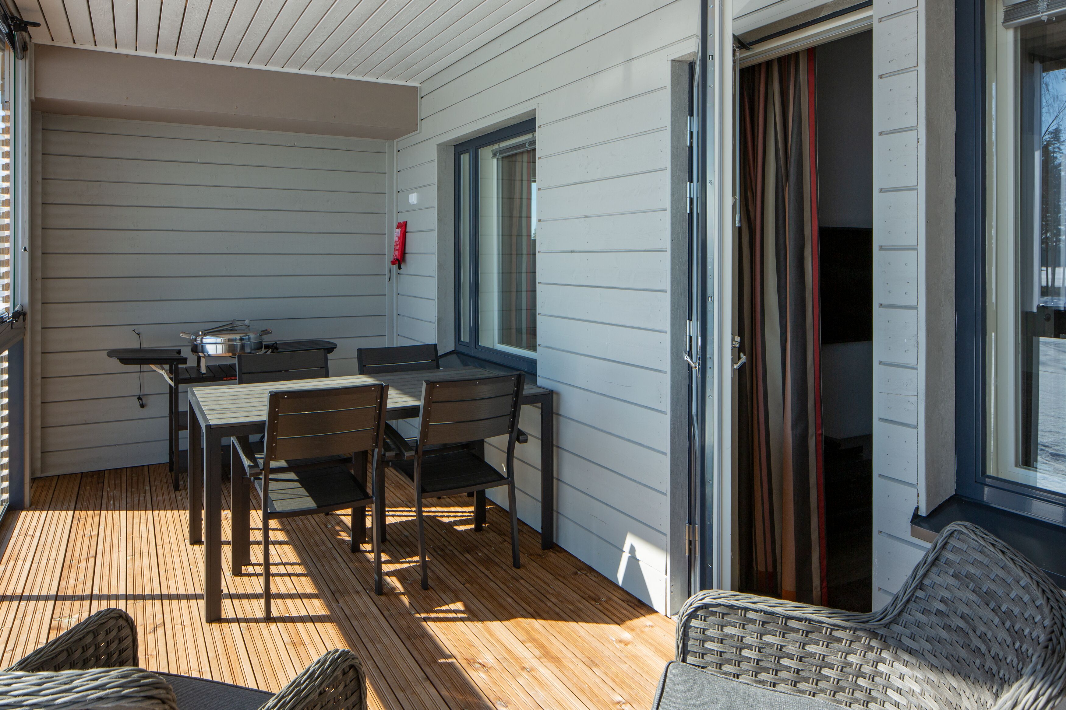 Un patio techado al aire libre con una mesa y sillas de comedor, un sofá de mimbre y una puerta corrediza de vidrio que da a un espacio interior.