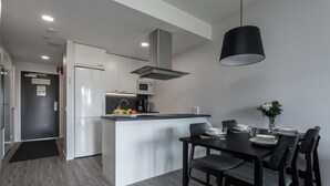Una cocina moderna con una isla central, armarios blancos, microondas integrado y una lámpara colgante negra.