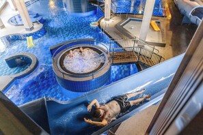 Una persona se desliza por un tobogán acuático en un área de piscina con un jacuzzi y una escalera.