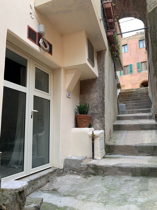 A narrow alleyway with a building entrance, a potted plant, and a staircase leading to another level. - Piccolo Appartemento Capoliveri (Capoliveri Isola'd Elba)