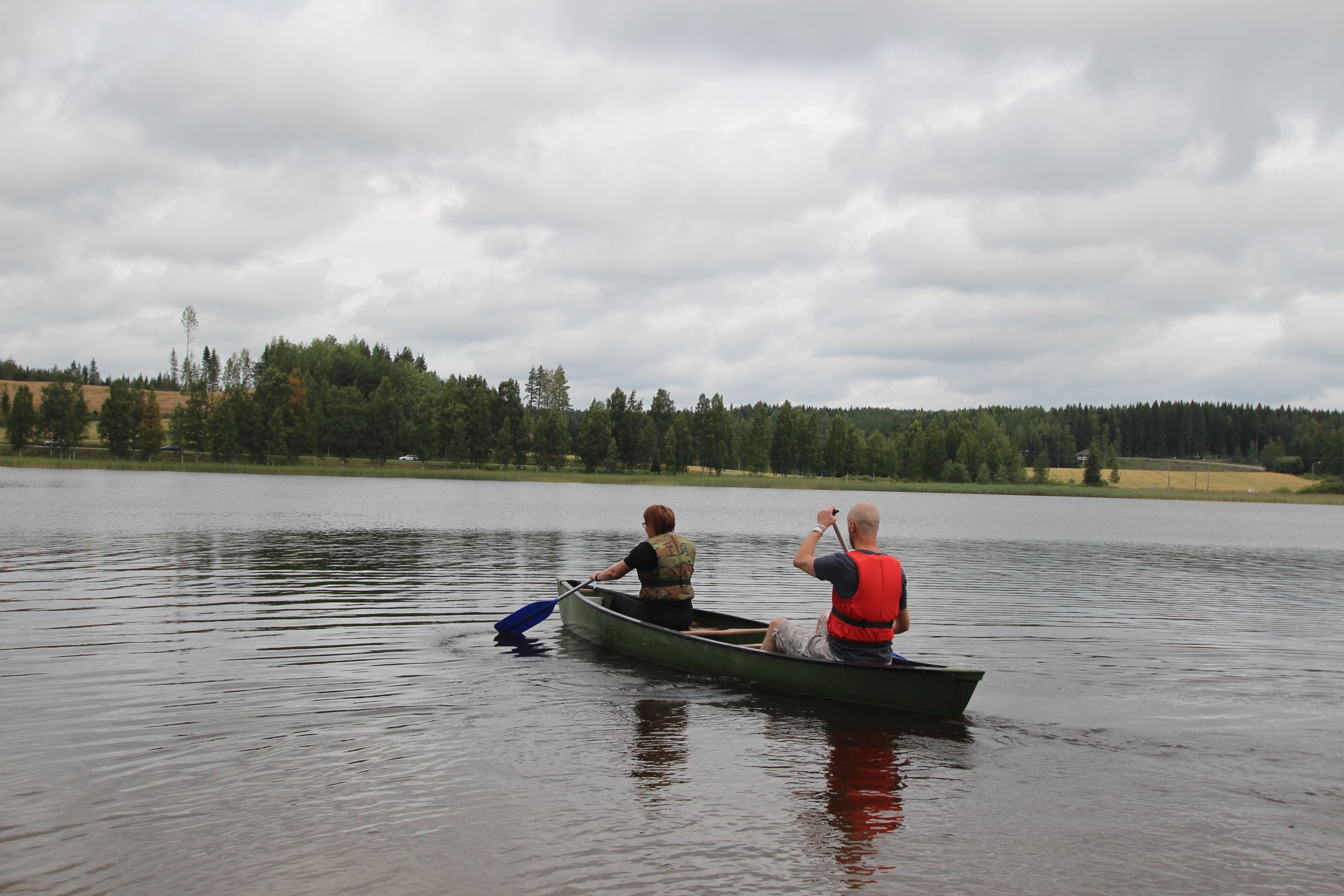 Kaksi ihmistä kanootissa tyynellä järvellä, taustalla metsäinen rantaviiva.