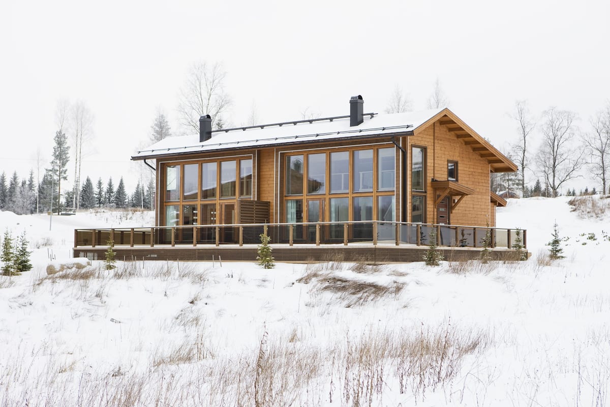Eine moderne Holz-Blockhütte mit großen Fenstern, einer Terrasse und verschneiter Landschaft.