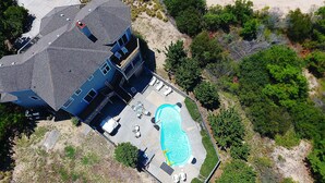 An aerial view of a two-story house with a swimming pool, a covered patio, and a fenced yard.