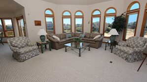 A living room with a sectional sofa, two armchairs, a coffee table, and a view of a residential area through large arched windows.