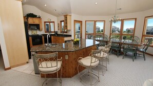 A spacious kitchen with a central island, wooden cabinets, and a dining area with chairs and a table.