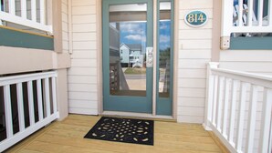 Une entrée de maison avec une porte de couleur turquoise, une plaque portant le numéro « 814 », et une terrasse en bois avec un paillasson noir.
