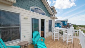 Une terrasse en bois avec deux fauteuils Adirondack turquoise, une petite table et un ensemble de mobilier de jardin blanc.
