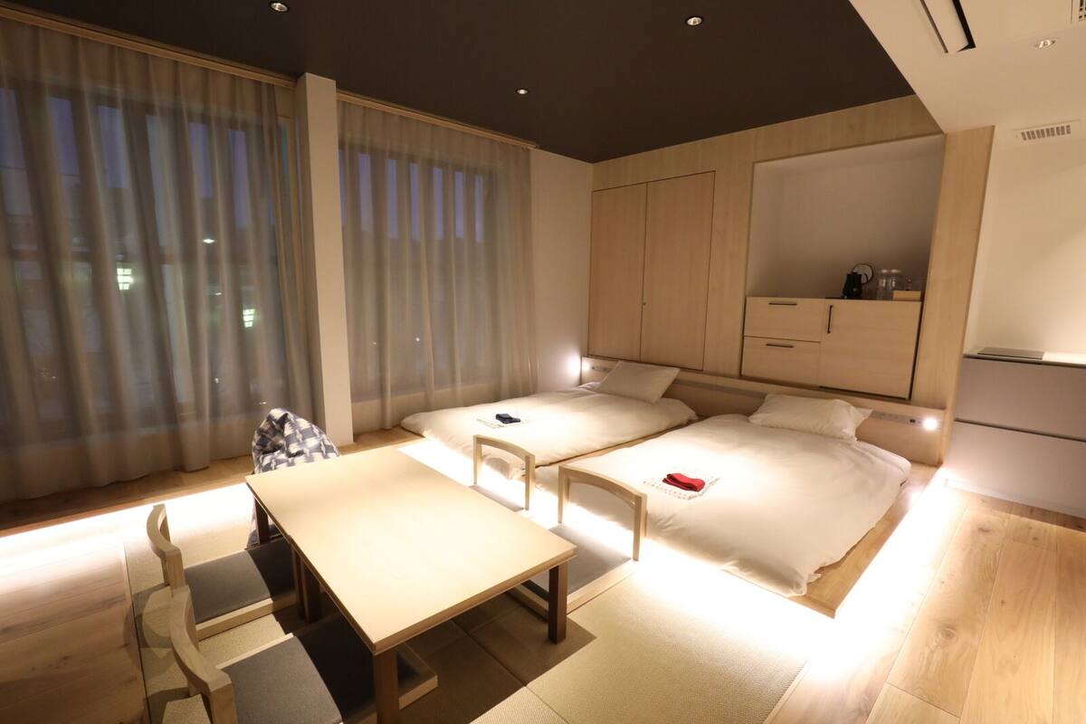 A modern hotel room with a large bed, a small desk, and a window with sheer curtains.