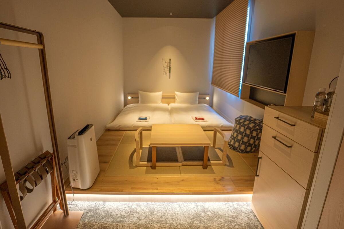 A compact hotel room with a bed, bedside table, TV, and a small kitchenette.
