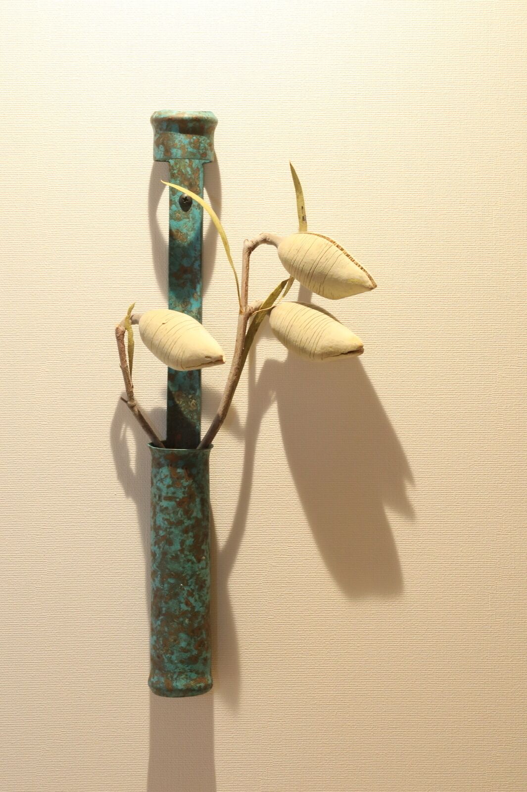 A vase with a rustic, weathered texture and a plant with elongated leaves.