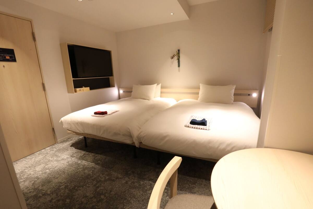 A hotel room with a double bed, a bedside table, a small desk, a chair, a TV mounted on the wall, and a door.