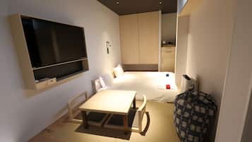 Een compacte hotelkamer met een bed, een klein tafeltje, een aan de muur bevestigde televisie en een kitchenette.