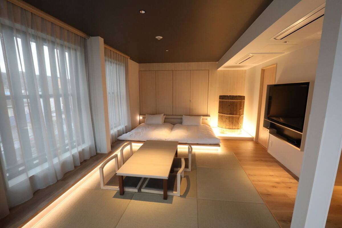 A modern bedroom with a bed, bedside tables, a TV, and a large window with curtains.