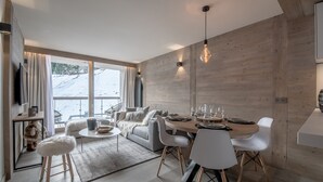 A modern living room with a dining area, large windows, and a view of a snowy landscape. - Winter Courchevel -- Phoenix 603 (Courchevel)