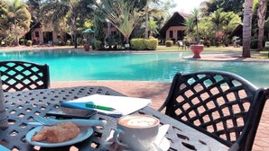 A poolside table with a plate of food, a cup of coffee, and a notebook. - Sandy's Creations Resort (Lusaka)