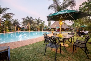 A poolside area with a brick pathway, outdoor seating, and umbrellas. - Sandy's Creations Resort (Lusaka)
