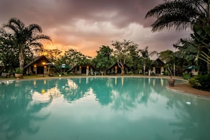 Ein friedlicher Poolbereich mit Sonnenuntergangsblick, umgeben von Palmen und kleinen Hütten.