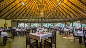 An indoor dining area with tables set for multiple guests, a high ceiling with a wooden framework, and natural light coming through the windows. - Sandy's Creations Resort (Lusaka)