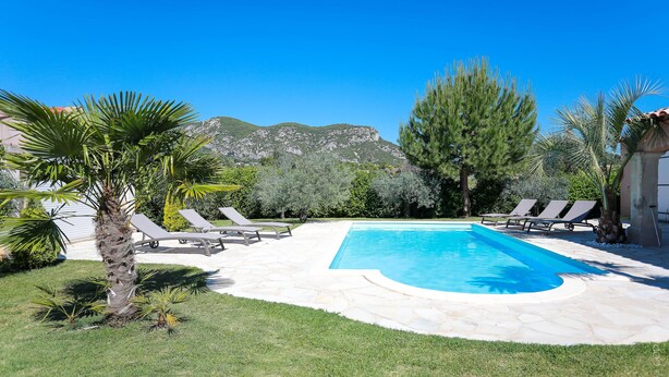 Una piscina con lettini, circondata da erba e palme, con montagne sullo sfondo.