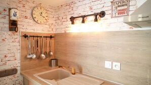 Una cucina con un piano di lavoro in legno, un appendiabiti per utensili, una sveglia e un cartello al muro.
