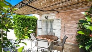 Una veranda esterna con un tavolo rotondo in legno, sedie in metallo, un tenda in bambù e una porta bianca con una finestra.