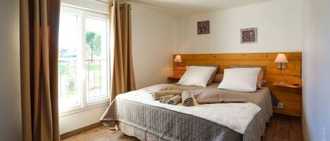 A bedroom with a wooden headboard, two bedside lamps, a bed with a quilted cover, and a window with curtains.