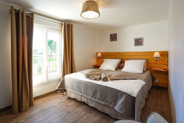 A bedroom with a wooden headboard, two bedside lamps, a bed with a quilted cover, and a window with curtains.