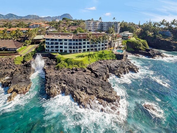 A coastal hotel with a rocky shoreline, a pool, and a view of the ocean.