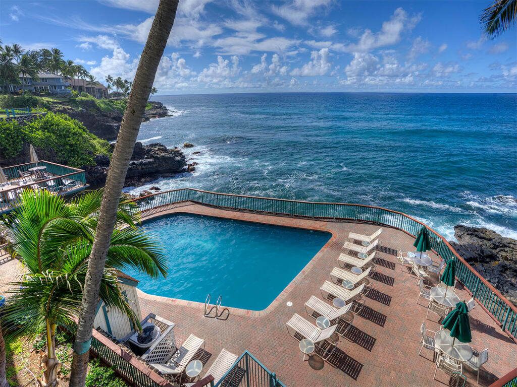 A pool area with lounge chairs and umbrellas, overlooking a rocky coastline and ocean.