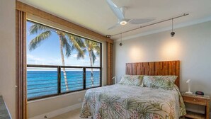 Ein Schlafzimmer mit großem Fenster und Meerblick, einem Deckenventilator und einem Holz-Kopfteil.