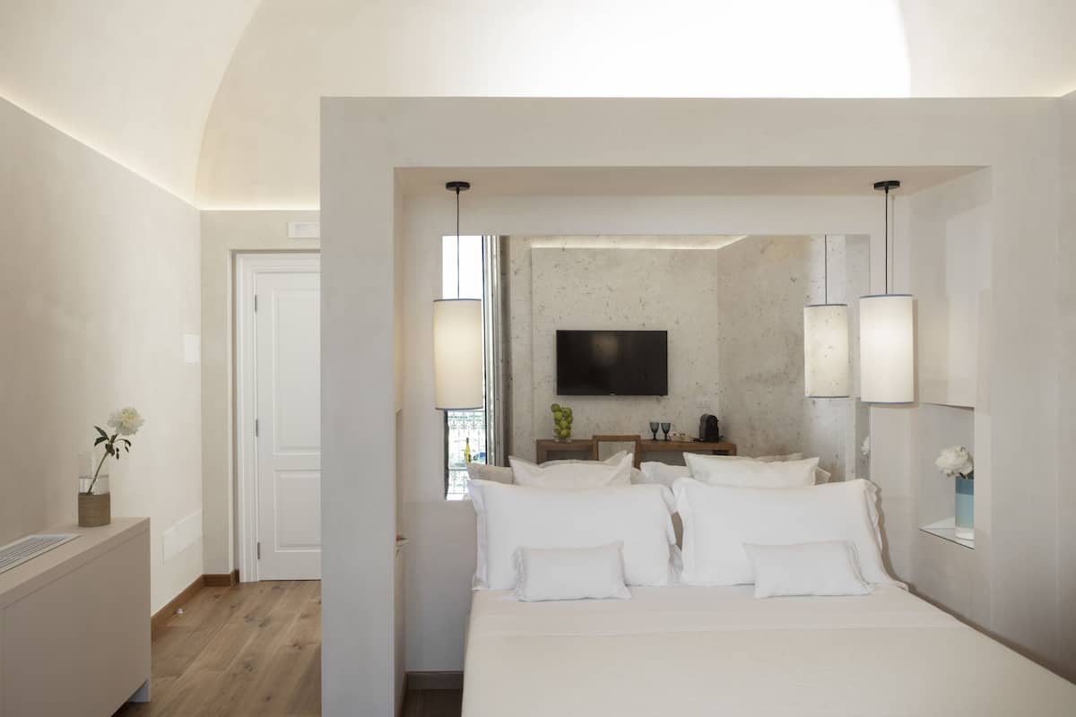 Una habitación de hotel moderna con una cama grande, un televisor de pantalla plana en la pared y una mesita con un jarrón de flores.