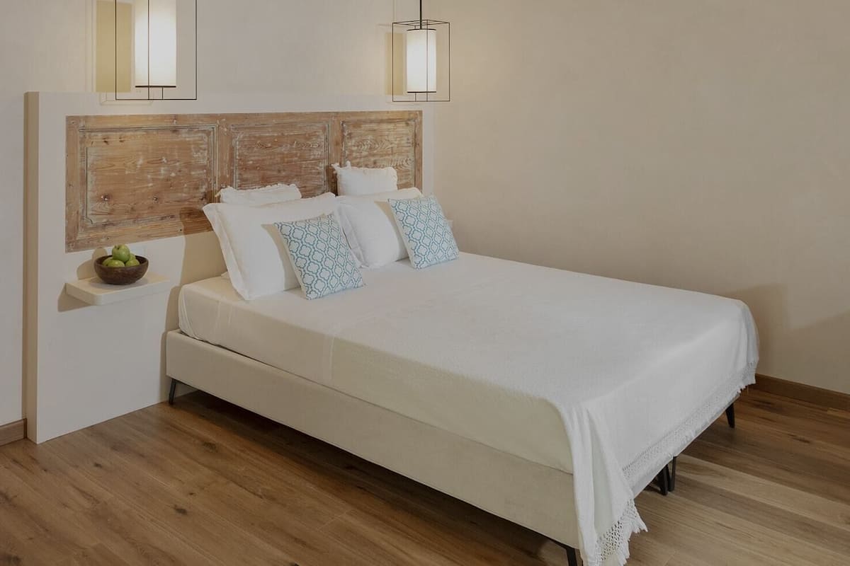 Un dormitorio con cabecera de madera, cama blanca y suelo de madera.