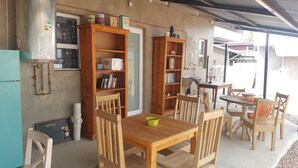 Un rincón comedor exterior acogedor con mobiliario de madera, una mesa con un cuenco verde y dos estanterías de madera llenas de libros y utensilios de cocina.